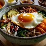 Bibimbap Rezept: Eine bunte Schüssel mit Reis, Gemüse, einem Spiegelei und Gochujang-Soße.